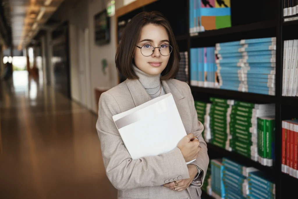 University student holding study documents in a library while building an academic profile.